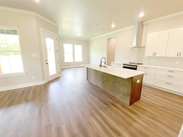 kitchen featuring light hardwood / wood-style flooring, stainless steel electric stove, wall chimney range hood, and a kitchen island with sink