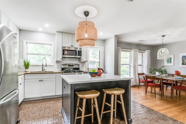 kitchen with stainless steel appliances, white cabinetry, hanging light fixtures, and a healthy amount of sunlight