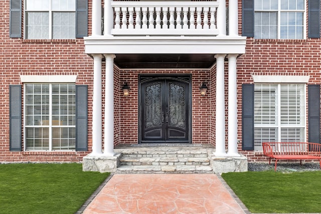 view of exterior entry featuring a balcony, brick siding, and french doors