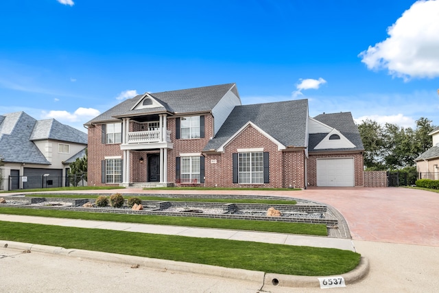 view of front of house with concrete driveway, brick siding, fence, and a balcony