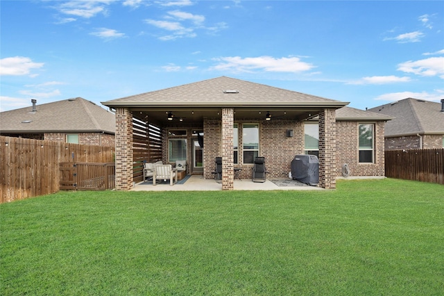 back of house with a fenced backyard, a shingled roof, a lawn, and a patio