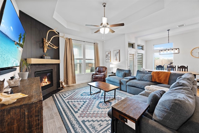 living room with a tray ceiling, ceiling fan, and light hardwood / wood-style floors