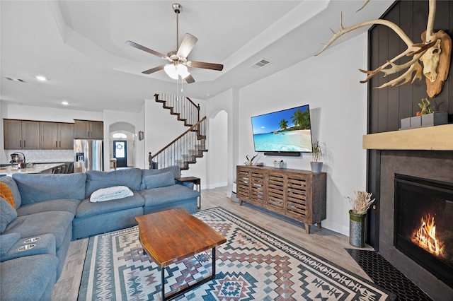 living room featuring light hardwood / wood-style flooring, ceiling fan, sink, and a raised ceiling