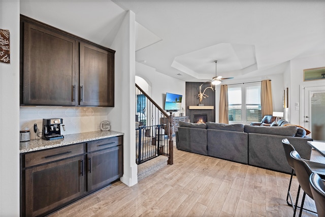 interior space with ceiling fan, a fireplace, light stone countertops, and dark brown cabinets