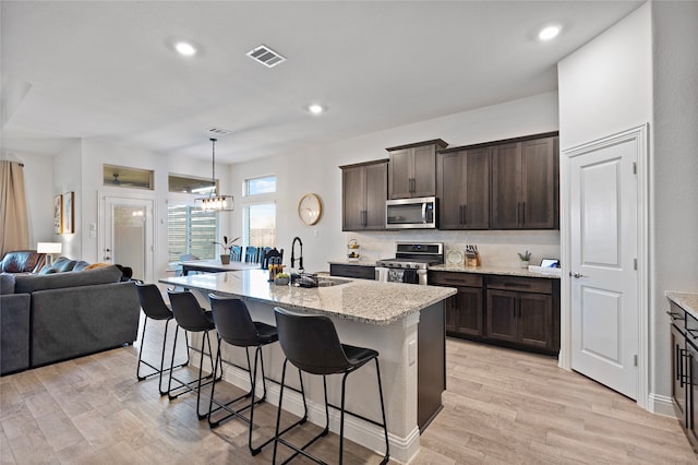 kitchen featuring light wood-type flooring, a kitchen breakfast bar, an inviting chandelier, sink, and appliances with stainless steel finishes