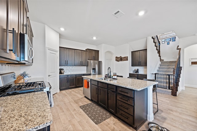 kitchen with light hardwood / wood-style flooring, appliances with stainless steel finishes, sink, a kitchen bar, and a kitchen island with sink