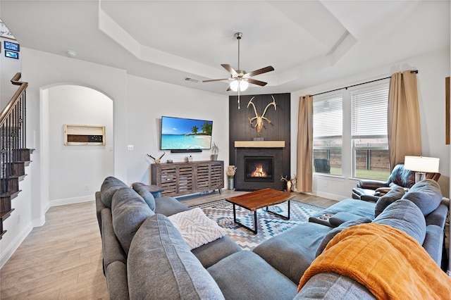 living room featuring a fireplace, a raised ceiling, light hardwood / wood-style flooring, and ceiling fan