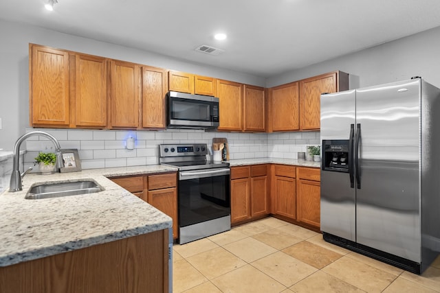 kitchen featuring light tile patterned floors, light stone countertops, stainless steel appliances, sink, and decorative backsplash