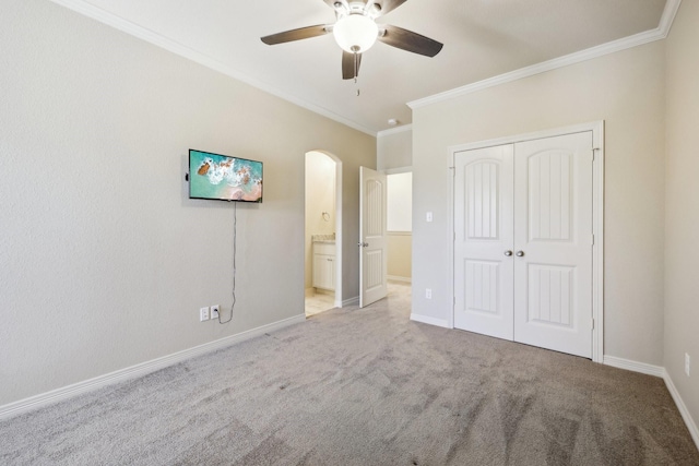 unfurnished bedroom featuring ceiling fan, connected bathroom, ornamental molding, light colored carpet, and a closet