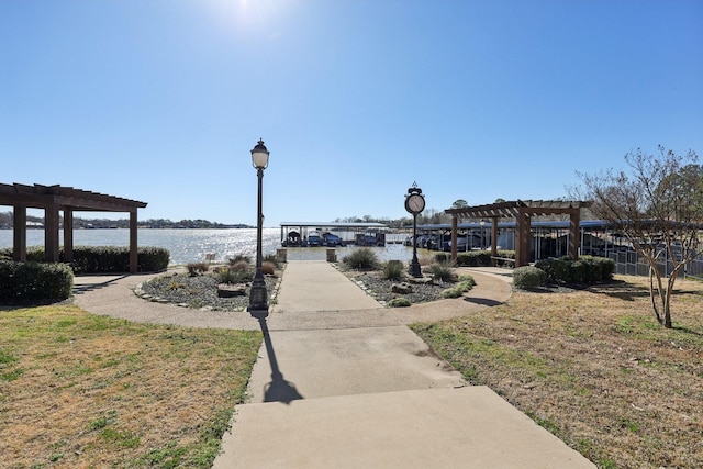 view of property's community with a yard, a pergola, and a water view