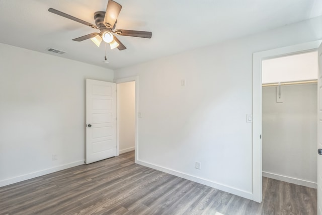 unfurnished bedroom featuring ceiling fan, a walk in closet, a closet, and hardwood / wood-style flooring