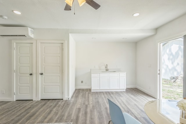 unfurnished living room featuring ceiling fan, sink, an AC wall unit, and light hardwood / wood-style flooring