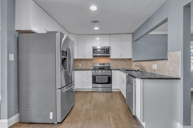 kitchen with dark stone counters, white cabinetry, light hardwood / wood-style flooring, sink, and appliances with stainless steel finishes