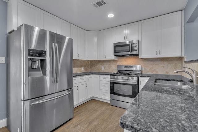 kitchen with white cabinets, dark stone countertops, appliances with stainless steel finishes, light hardwood / wood-style floors, and sink