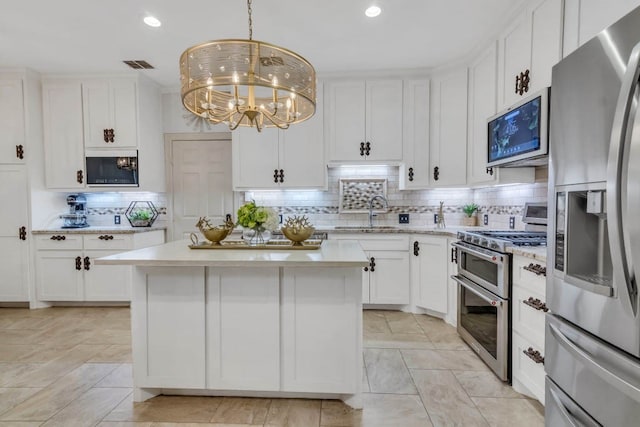 kitchen featuring white cabinets, backsplash, appliances with stainless steel finishes, a chandelier, and a kitchen island