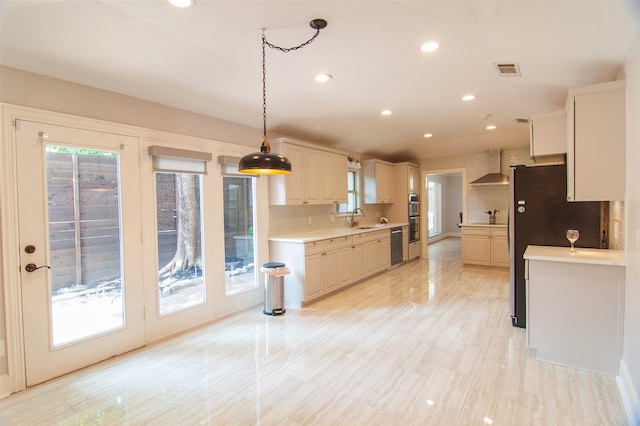 kitchen with wall chimney exhaust hood, pendant lighting, sink, and a healthy amount of sunlight