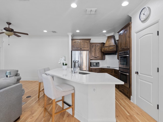 kitchen with stainless steel appliances, sink, an island with sink, and light hardwood / wood-style flooring