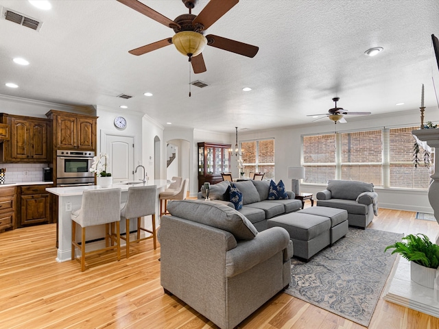 living room with ceiling fan, light hardwood / wood-style floors, a textured ceiling, and ornamental molding