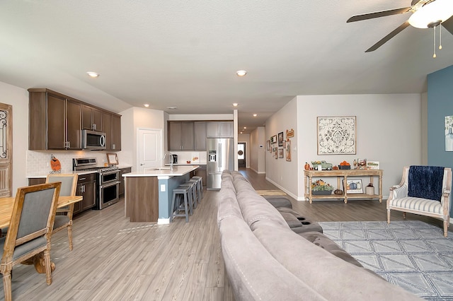 living room with a textured ceiling, light hardwood / wood-style floors, ceiling fan, and sink