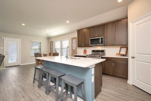 kitchen with sink, decorative backsplash, an island with sink, light hardwood / wood-style floors, and stainless steel appliances