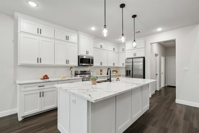 kitchen with a kitchen island with sink, dark wood-type flooring, stainless steel appliances, hanging light fixtures, and white cabinetry