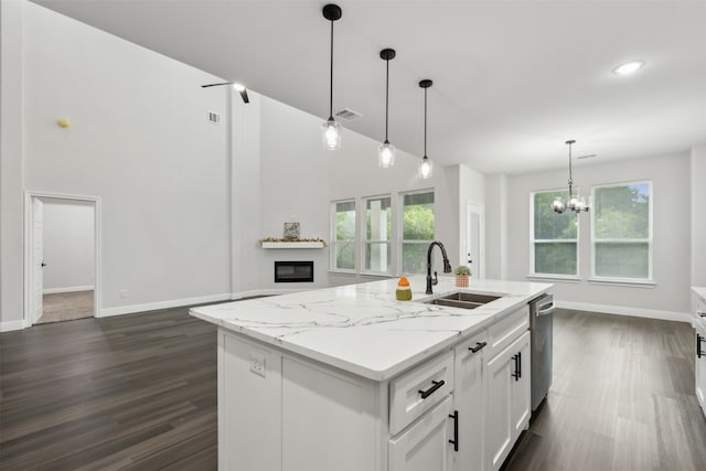 kitchen featuring light stone countertops, decorative light fixtures, a kitchen island with sink, sink, and white cabinets