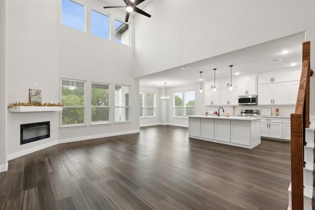 unfurnished living room featuring ceiling fan with notable chandelier, dark hardwood / wood-style flooring, sink, and a high ceiling