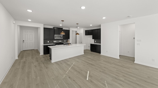 kitchen with sink, light hardwood / wood-style flooring, a kitchen island with sink, stainless steel appliances, and tasteful backsplash