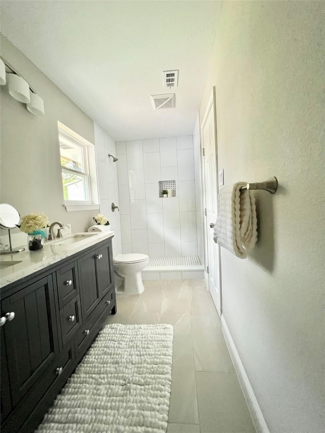 bathroom with a tile shower, tile patterned flooring, vanity, and toilet