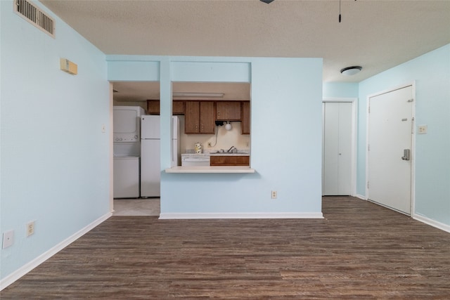 unfurnished living room with hardwood / wood-style flooring, a textured ceiling, and stacked washer / drying machine