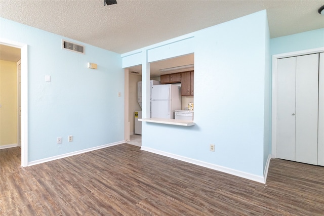 spare room featuring a textured ceiling, hardwood / wood-style floors, and stacked washer / drying machine