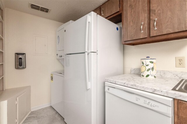 104 Harbor Dr Unit 111, Runaway Bay, TX 76426 - kitchen featuring white appliances, stacked washing machine and dryer, light countertops, brown cabinetry, and light marble finish flooring