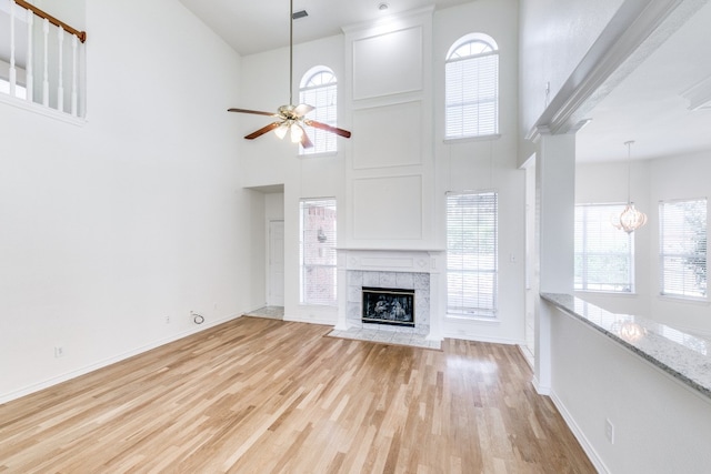 unfurnished living room featuring a high ceiling, ceiling fan with notable chandelier, light wood-type flooring, and a fireplace