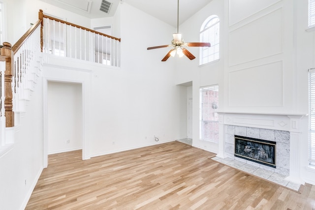 unfurnished living room featuring a high ceiling, ceiling fan, a tiled fireplace, and light wood-type flooring