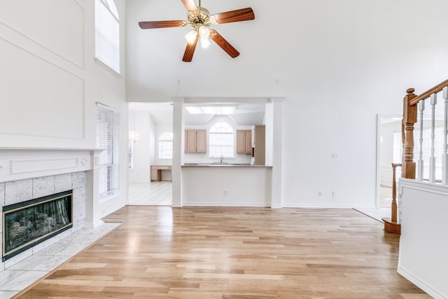 unfurnished living room with a healthy amount of sunlight, ceiling fan, light wood-type flooring, and a tile fireplace