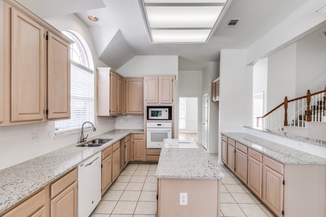 kitchen with white appliances, light brown cabinetry, light stone counters, sink, and a kitchen island