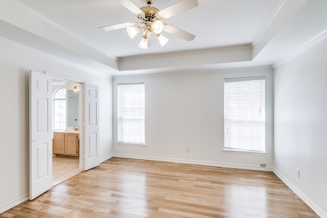 unfurnished bedroom featuring a raised ceiling, light hardwood / wood-style floors, crown molding, ensuite bath, and ceiling fan