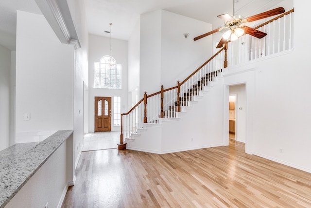 entrance foyer featuring a towering ceiling, ceiling fan with notable chandelier, and light wood-type flooring