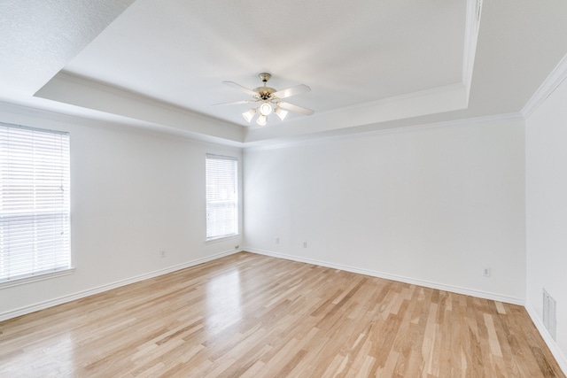 empty room with light wood-type flooring, a tray ceiling, and ceiling fan