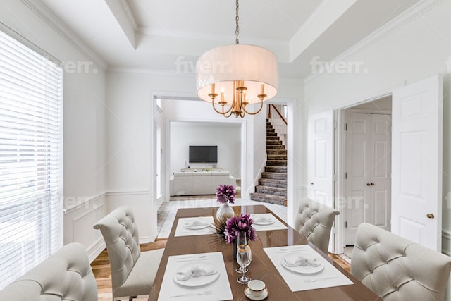 dining space with a tray ceiling, ornamental molding, wood-type flooring, and an inviting chandelier