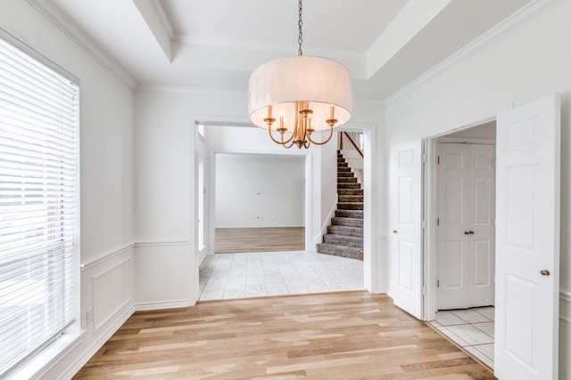 unfurnished dining area featuring a tray ceiling, a chandelier, light hardwood / wood-style floors, and ornamental molding