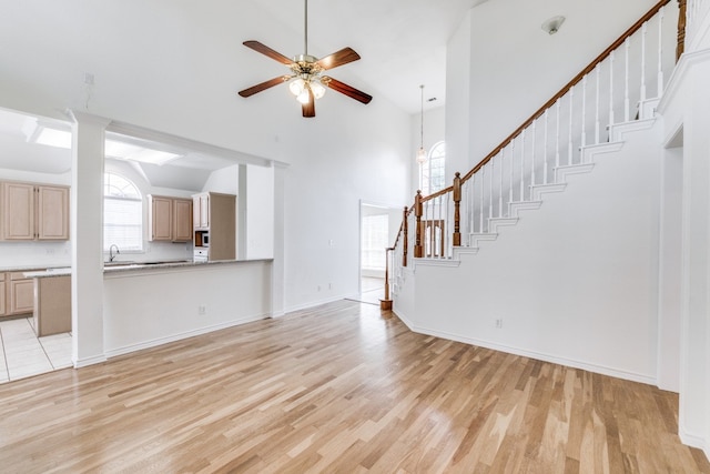 unfurnished living room featuring high vaulted ceiling, ceiling fan, sink, and light wood-type flooring