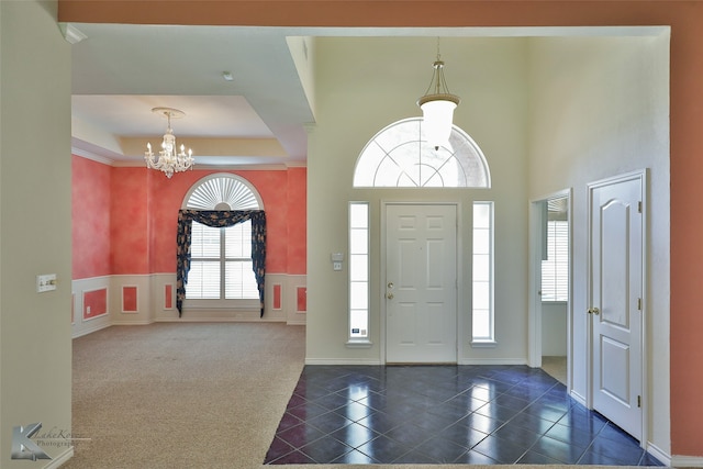 foyer entrance with dark carpet, a tray ceiling, a notable chandelier, and a healthy amount of sunlight