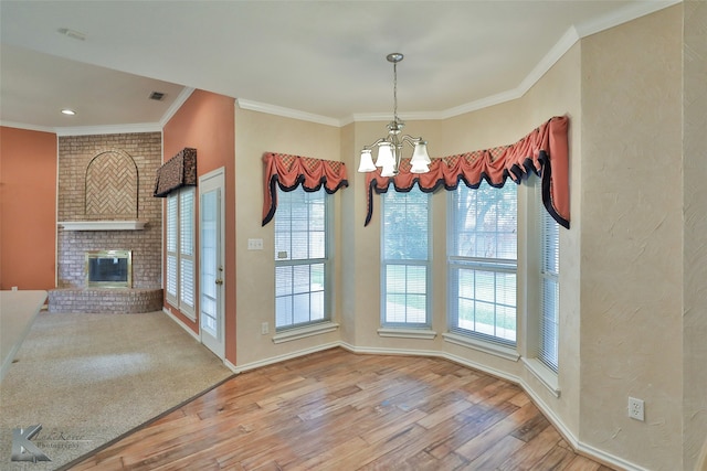 unfurnished dining area with crown molding, a notable chandelier, hardwood / wood-style flooring, and a fireplace