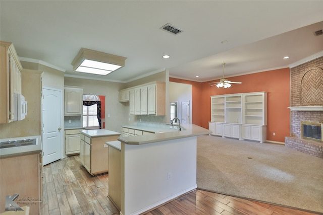 kitchen with ceiling fan, light hardwood / wood-style floors, kitchen peninsula, and a brick fireplace