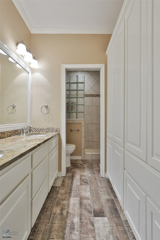 bathroom with hardwood / wood-style flooring, crown molding, toilet, a tile shower, and vanity