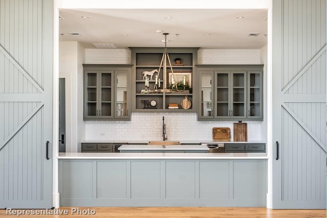 bar with light wood-type flooring, backsplash, sink, decorative light fixtures, and gray cabinets