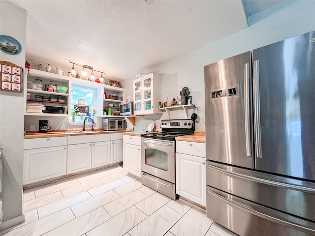 kitchen with butcher block counters, sink, white cabinetry, appliances with stainless steel finishes, and a textured ceiling