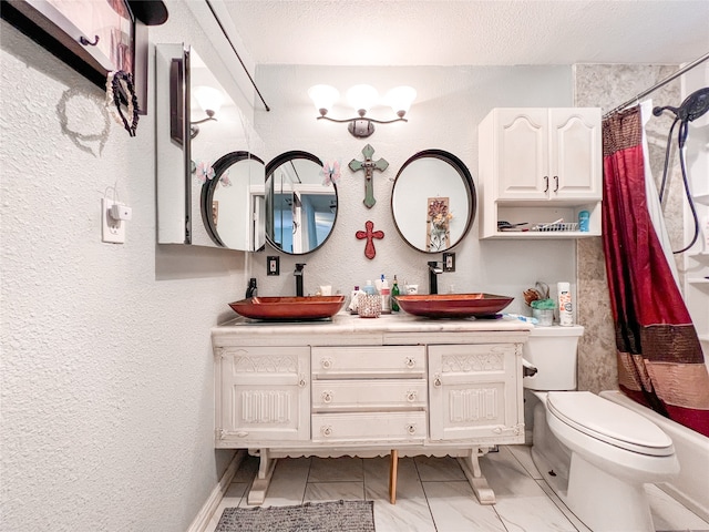 bathroom featuring a textured wall, double vanity, a sink, and toilet