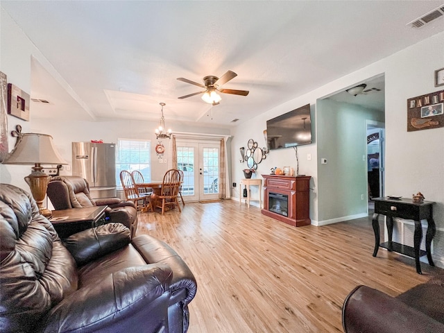 living room with light wood-style flooring, ceiling fan with notable chandelier, visible vents, baseboards, and a glass covered fireplace